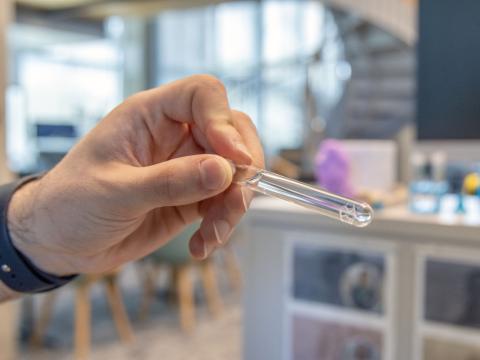 A small hexagonal 3D structure about the size of a human fingernail sits inside of a vial of water.