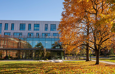 Landscape view of modern, newly-built Tykeson Hall building with two trees in fall folliage